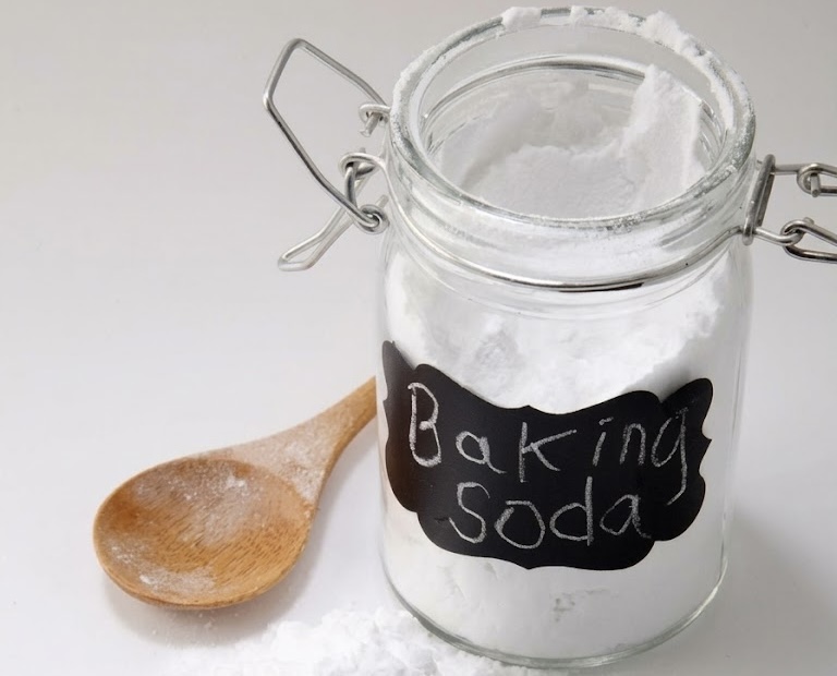 Clear glass jar containing baking soda powder, featuring a wooden spoon and black label
